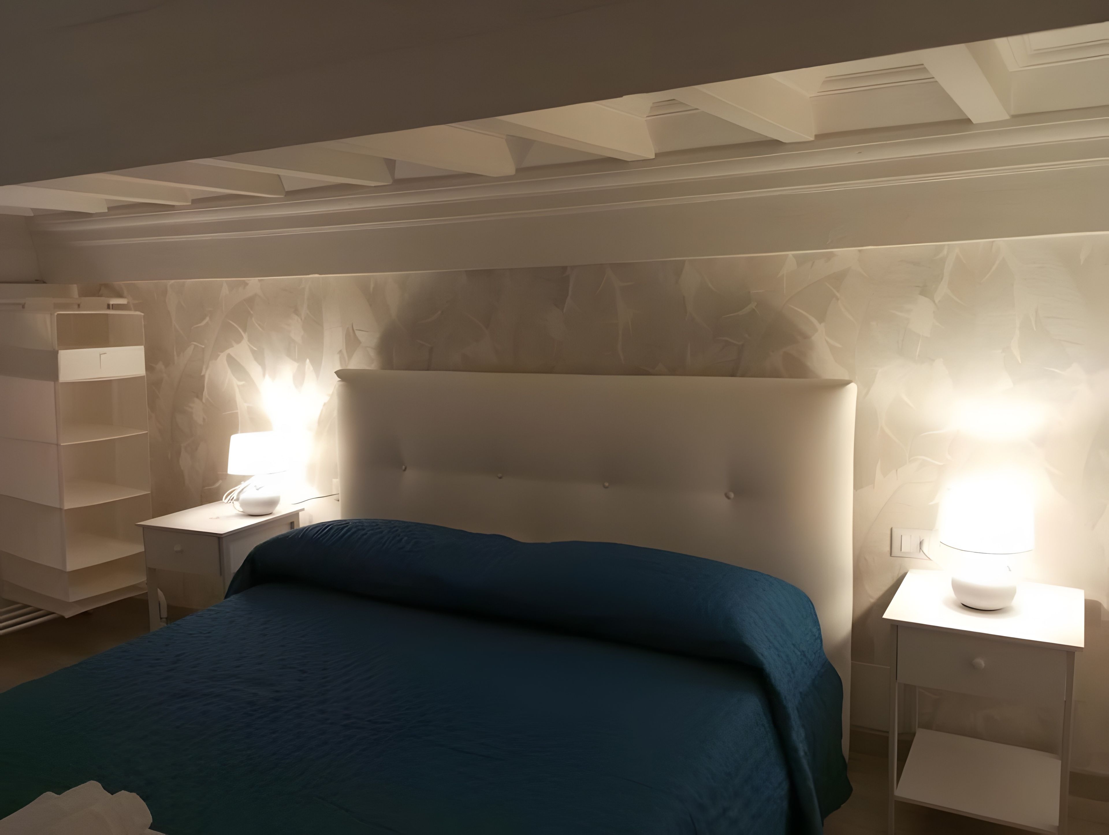 Une chambre avec un grand lit, deux tables de chevet et un mur orné d’un motif de feuilles.