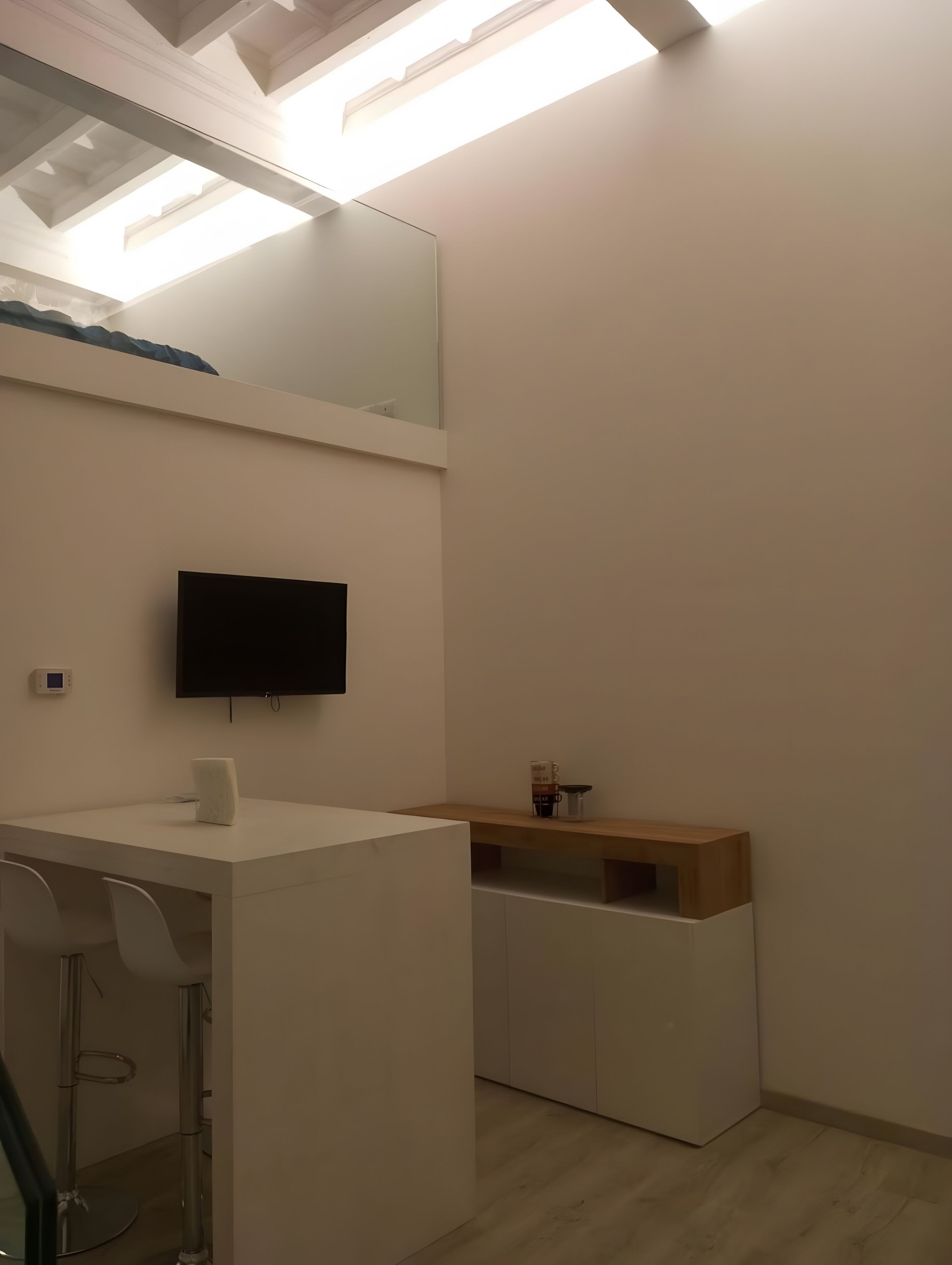 A modern bathroom with a white vanity, a mirror, a flat-screen TV, and a wooden shelf.