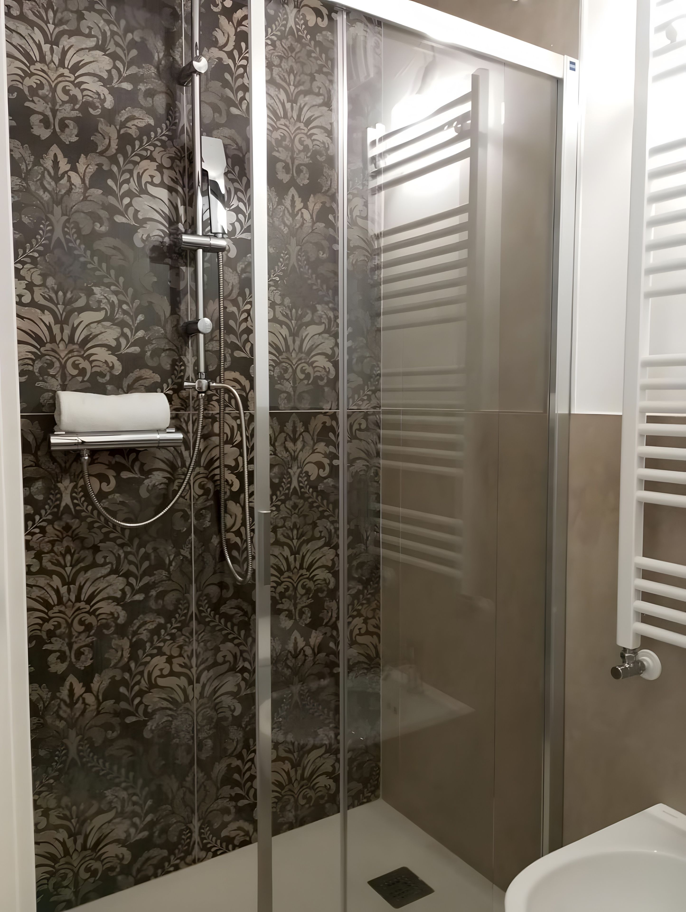 Cabina doccia con porta in vetro, asciugamano e water con porta rotolo carta igienica bianco.