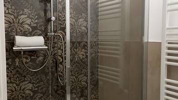 Cabina doccia con porta in vetro, asciugamano e water con porta rotolo carta igienica bianco.