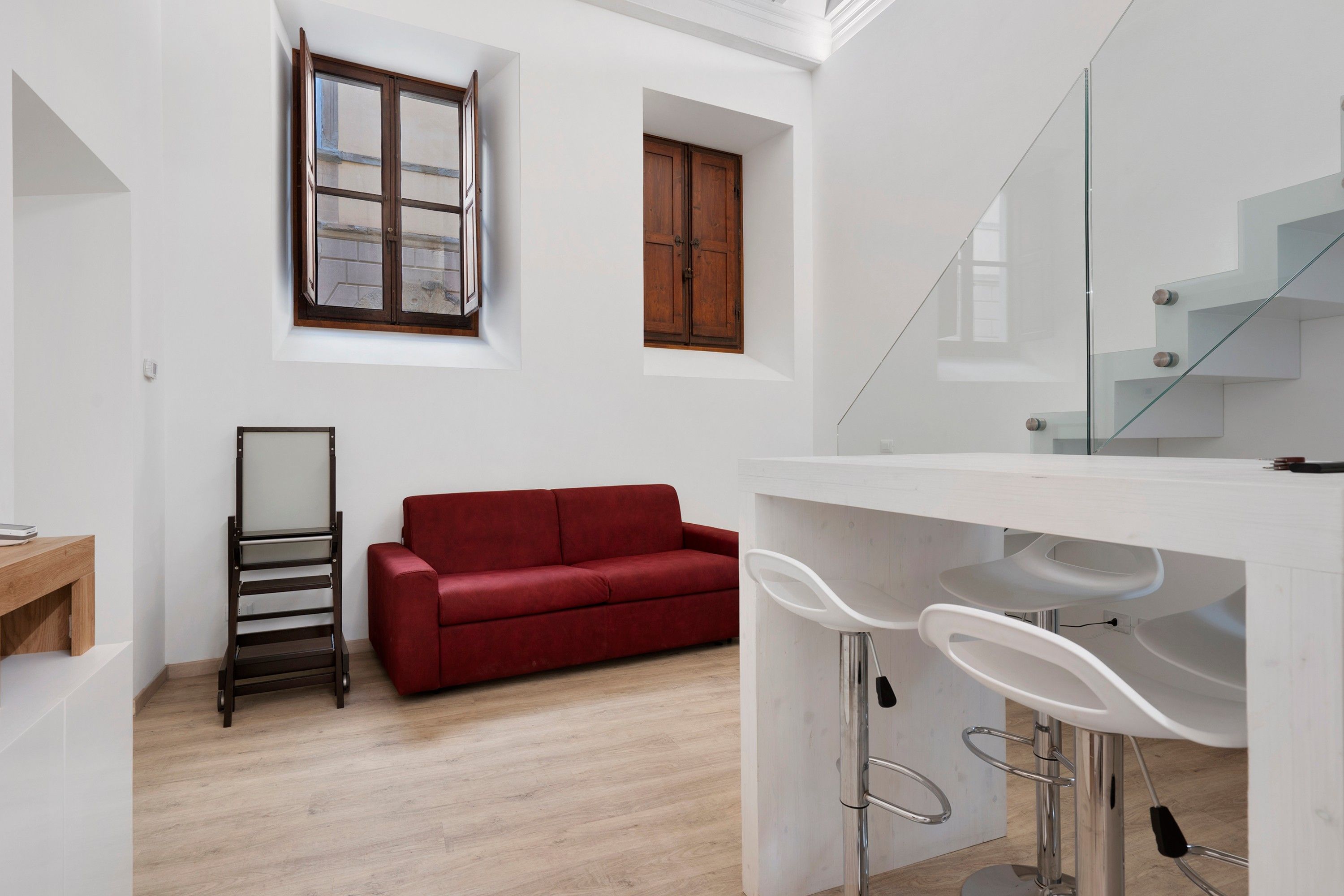 A modern interior with a red sofa, a white bar area with stools, a wooden ladder, and a staircase.