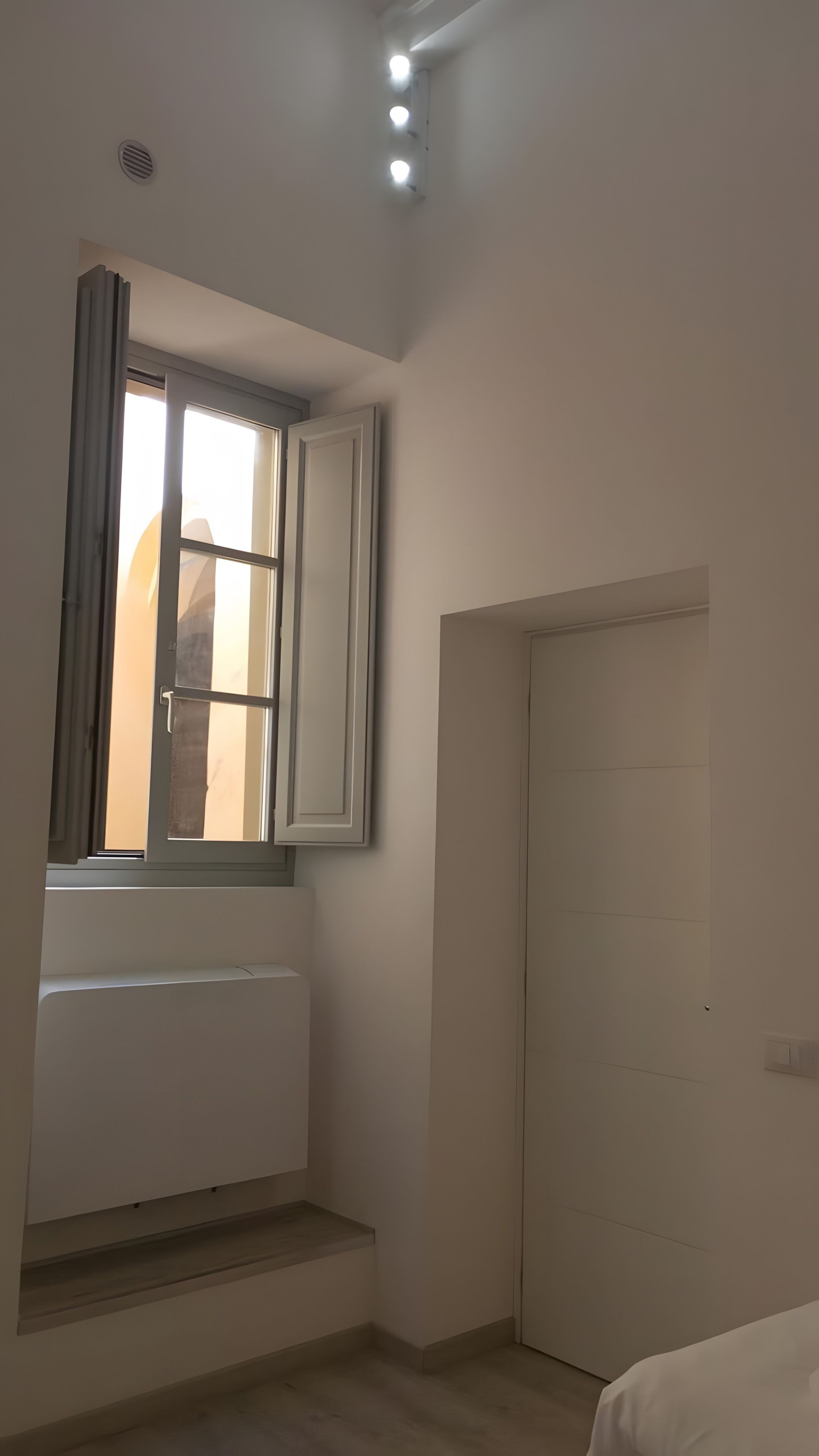 Una stanza con una finestra, un termosifone, una porta e un lampadario.