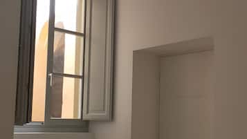 Una stanza con una finestra, un termosifone, una porta e un lampadario.