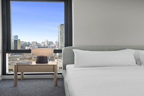 A hotel room with a bed, a nightstand with a lamp, and a view of a cityscape through a large window. - High-Rise 2-Bed Apartment Near Southbank (South Melbourne)