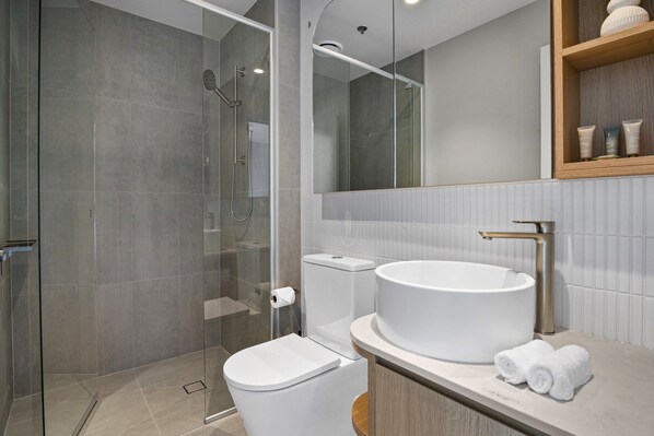 A modern bathroom with a glass-enclosed shower, a white toilet, and a round sink with a towel on the counter. - High-Rise 2-Bed Apartment Near Southbank (South Melbourne)