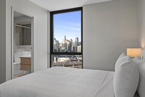 A hotel room with a large bed, a window with a city view, a bedside table, and a mirror. - High-Rise 2-Bed Apartment Near Southbank (South Melbourne)