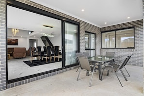 A modern interior with a glass partition, a dining area with a glass table and chairs, and a view of a living room with a sofa and chairs. - Family 5-Bed House Near Tarneit Central (Tarneit)