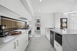 Une cuisine moderne avec des meubles blancs, une cuisinière en acier inoxydable et un sol en marbre.