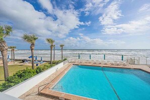 Ein Pool mit Blick auf den Ozean, umgeben von Palmen und Liegestühlen.