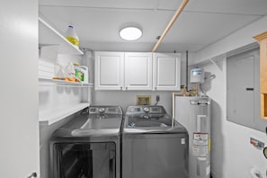 A laundry room with two front-loading washers, a water heater, and a shelf with cleaning supplies. - 8D Royal Atlantic 2/2 ocean view unit. (Daytona Beach Shores)