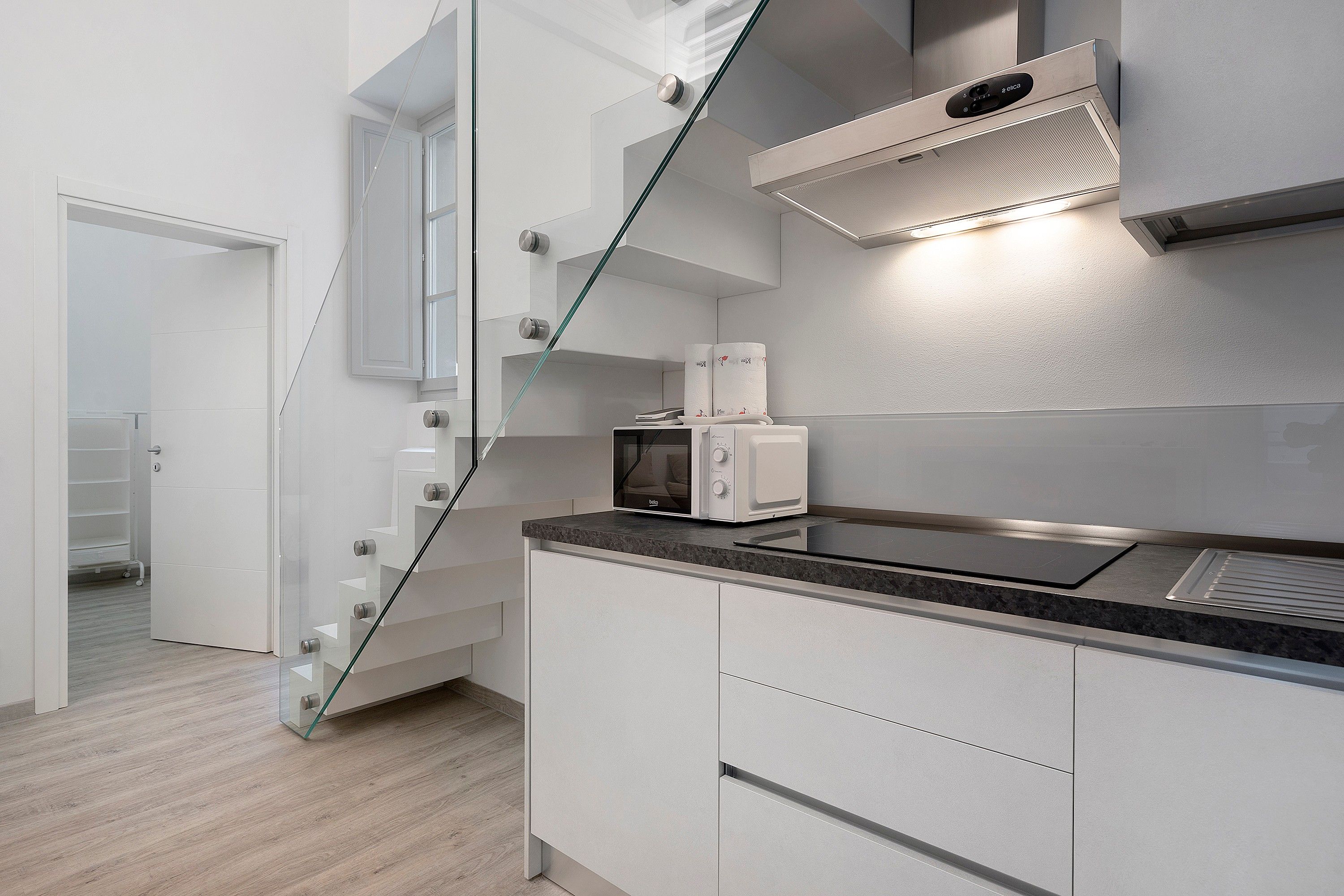 Una cucina moderna con forno a microonde integrato, una scala in vetro e un armadietto bianco.