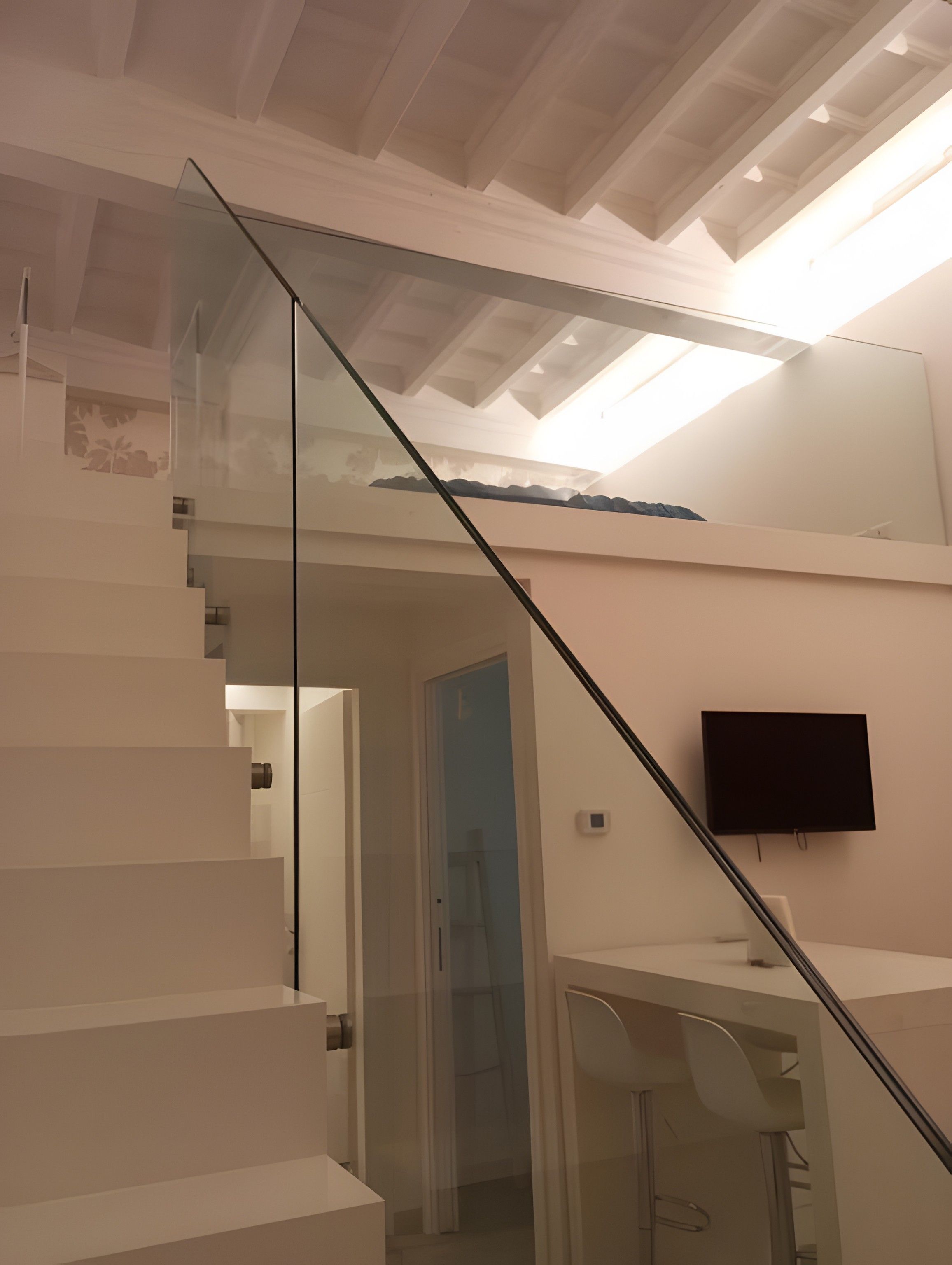 Eine moderne Treppe mit Glastrennwand, einer flachen Decke mit eingelassener Beleuchtung und einem an der Wand befestigten Fernseher.