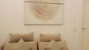 Une pièce avec un canapé beige, deux coussins et un grand tableau abstrait accroché au mur.