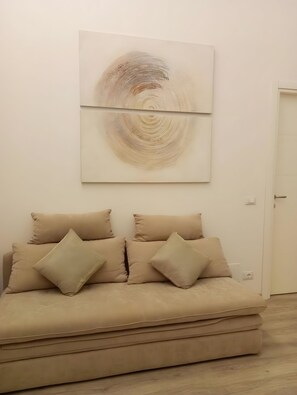 Ein Zimmer mit einem beigen Sofa, zwei Kissen und einem großen abstrakten Gemälde an der Wand.