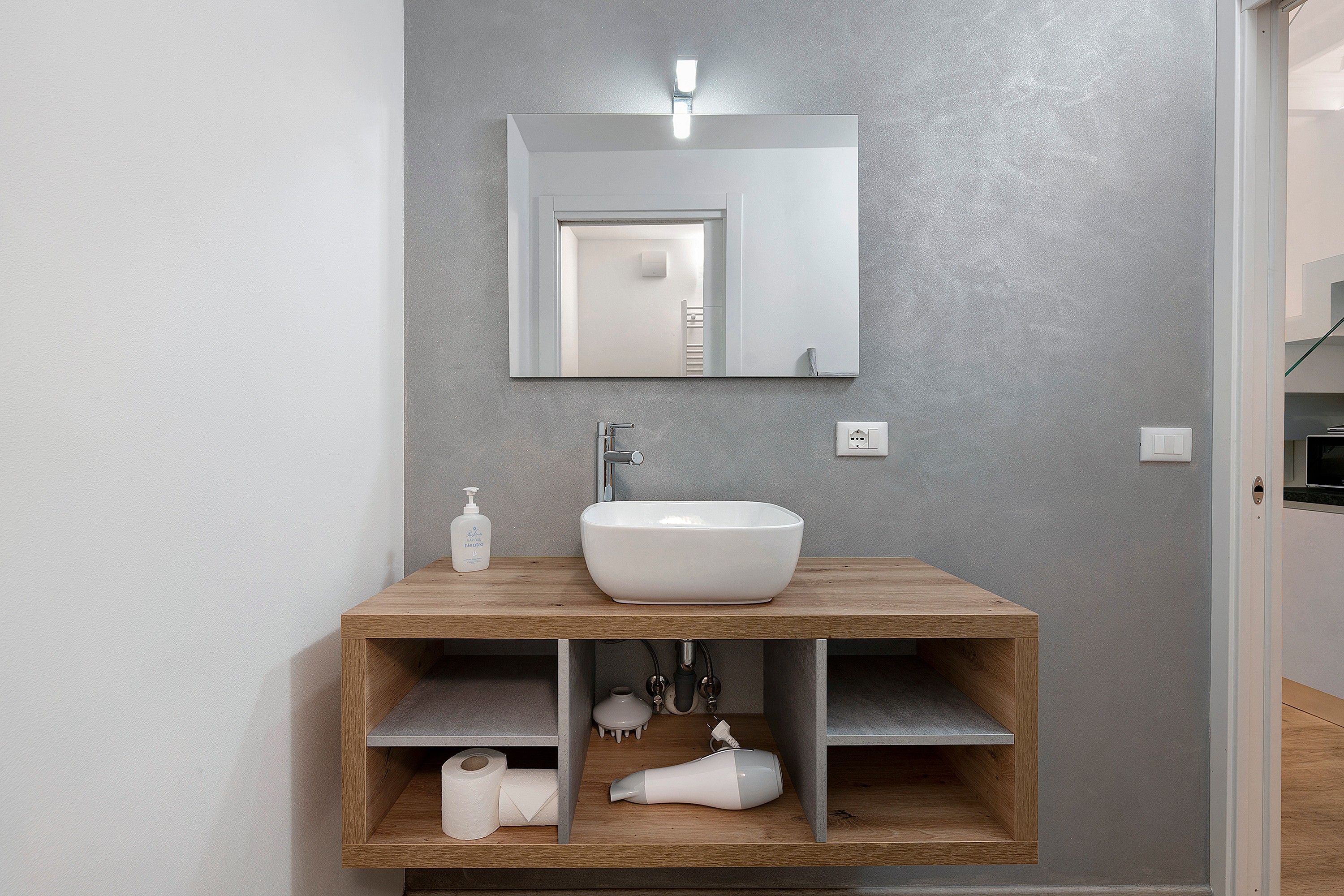 Ein Badezimmer mit einem weißen Waschbecken, einem Spiegel und einer Holzausstattung mit Regalen.