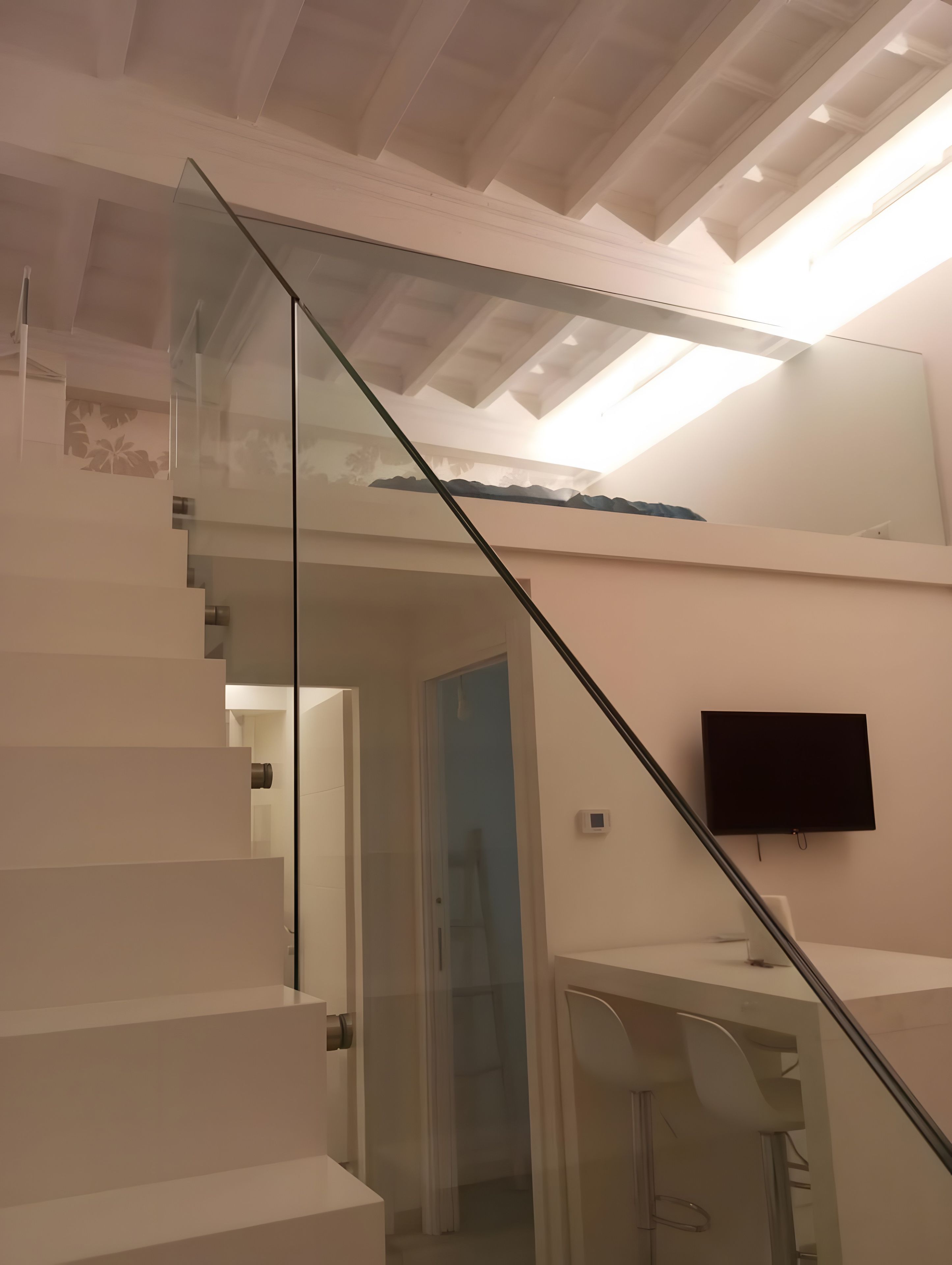 Un escalier moderne avec des rampes en verre mène au deuxième étage. Un téléviseur à écran plat est fixé au mur.