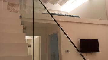 Un escalier moderne avec des rampes en verre mène au deuxième étage. Un téléviseur à écran plat est fixé au mur.