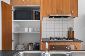 A kitchen with wooden cabinets, a microwave, a gas stove, and a sink. - Bright 1-Bed House Near Thornbury Cafes (Thornbury)