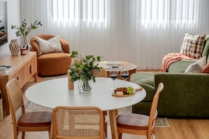A modern living room with a round dining table, two chairs, a sofa, and a coffee table with a floral centerpiece. - Olive & Ochre | Warm Coastal Retreat (Shoalwater)