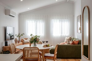 A modern living room with a dining area, featuring a sofa, chairs, a table, and a TV. - Olive & Ochre | Warm Coastal Retreat (Shoalwater)