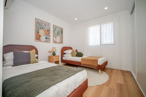 A bedroom with two beds, a nightstand, a lamp, and artwork on the wall. - Olive & Ochre | Warm Coastal Retreat (Shoalwater)