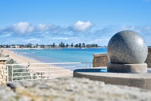 A coastal view with a stone monument, a sandy beach, and a clear blue sea. - Olive & Ochre | Warm Coastal Retreat (Shoalwater)