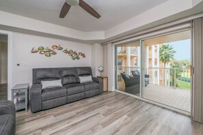 A spacious living room with a grey leather sofa, a small side table, and a decorative wall piece. - A301 Links at Harbour Village 3/3 condo. (Ponce Inlet)