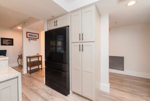 Eine moderne Küche mit einem schwarzen Kühlschrank, weißen Schränken und einem Holzes Esstisch.