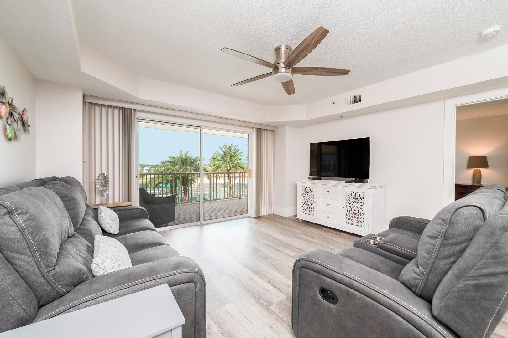 A modern living room with grey leather sofas, a flat-screen TV, and a ceiling fan.