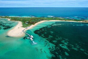An aerial view of a coastal area with a sandy beach, clear turquoise waters, and a pier extending into the sea. - Beachside 4-Bed House With Pool In Warnbro (Warnbro)