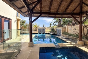 A swimming pool with a pergola overhead, surrounded by stone walls and tropical plants. - Beachside 4-Bed House With Pool In Warnbro (Warnbro)