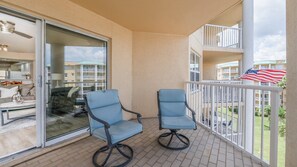 A balcony with two chairs, a glass door leading to a room, and a view of other buildings. - A506 Links South in Ponce Inlet, FL (Ponce Inlet)