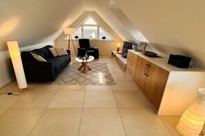 Een knus woongedeelte met een bank, een salontafel, een lamp, een televisie en een keuken met kastjes en een aanrecht.