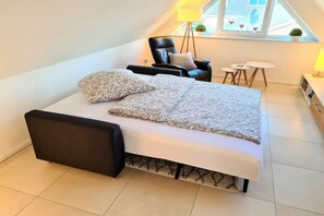 Quarto moderno com cama, poltrona, mesinha e abajur.