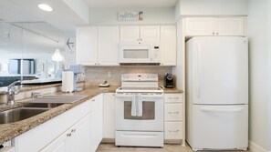A modern kitchen with white cabinetry, a built-in microwave, a stove, and a refrigerator. - #606 Atlantica Oceanfront 2/2 Condo. (Ponce Inlet)