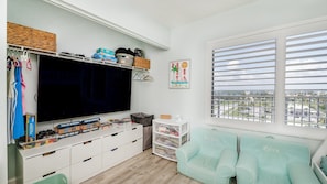 A room with a television, storage units, a window with blinds, and a view of a cityscape. - #606 Atlantica Oceanfront 2/2 Condo. (Ponce Inlet)