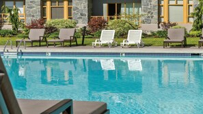 Una piscina con sillones de descanso y un edificio de piedra al fondo.