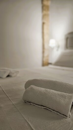 A neatly made bed with a folded towel and a visible wooden beam in the background. - Domus Sirii - Vacation Home in the Heart of Lecce's Historic Center (Lecce)