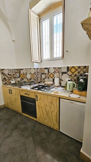 A kitchen with a tiled backsplash, a window, a sink, a stove, and a dishwasher. - Domus Sirii - Vacation Home in the Heart of Lecce's Historic Center (Lecce)