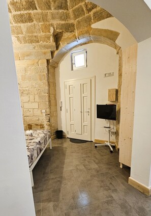 A room with a stone wall, a bed, a TV, and a door. - Domus Sirii - Vacation Home in the Heart of Lecce's Historic Center (Lecce)