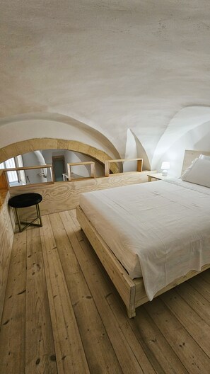 Une chambre avec un plancher en bois, un lit, une table de chevet, une chaise et un miroir.