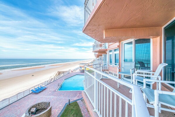 Un balcón con vista a la playa, una piscina y mobiliario exterior.
