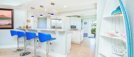 A modern kitchen with white cabinets, a central island, and blue bar stools.