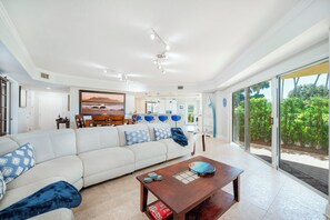A modern living room with a large sofa, a wooden coffee table, and a view of a garden through large sliding doors. - C103 Links North in Ponce Inlet, FL (Ponce Inlet)