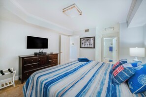 A bedroom with a bed, a dresser, a television, a framed picture, and a door leading to another room. - C103 Links North in Ponce Inlet, FL (Ponce Inlet)