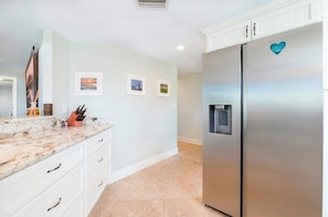 Una cocina con armarios blancos, un refrigerador de acero inoxidable y una encimera de mármol.