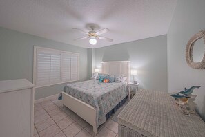 A bedroom with a bed, a nightstand, a lamp, a ceiling fan, and a wall-mounted mirror. - D-407 Links North in Ponce Inlet, FL (Ponce Inlet)