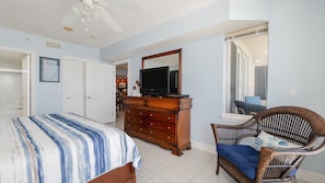 A bedroom with a bed, dresser, television, chair, and a window with a view. - Dimucci Twin Towers 1503 (Daytona Beach Shores)