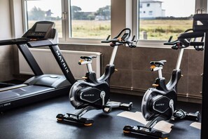 Ein Fitnessraum mit Ergometer und Laufband, großen Fenstern und Blick ins Freie.