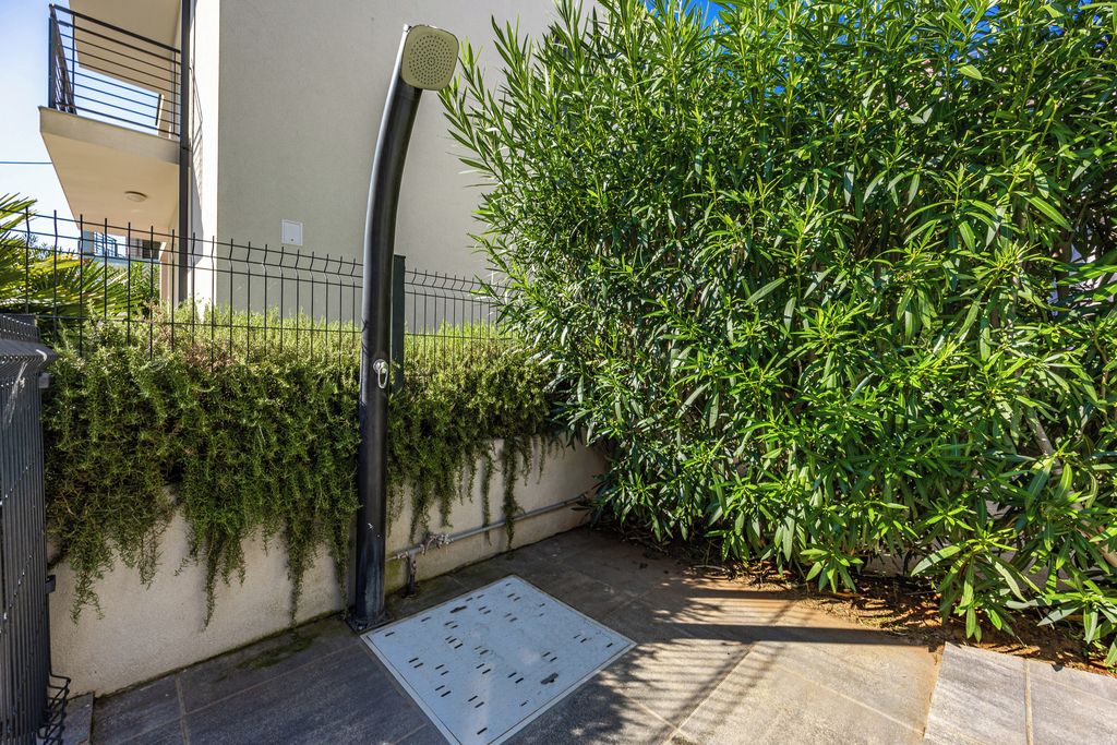A paved pathway with a metal grate, a metal fence, and a bushy green hedge.